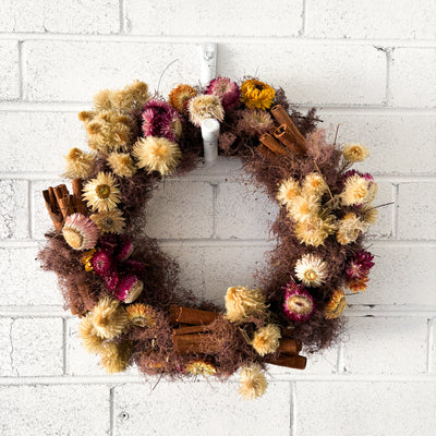 Decorative wreath with dried flowers and cinnamon sticks on a white brick wall.