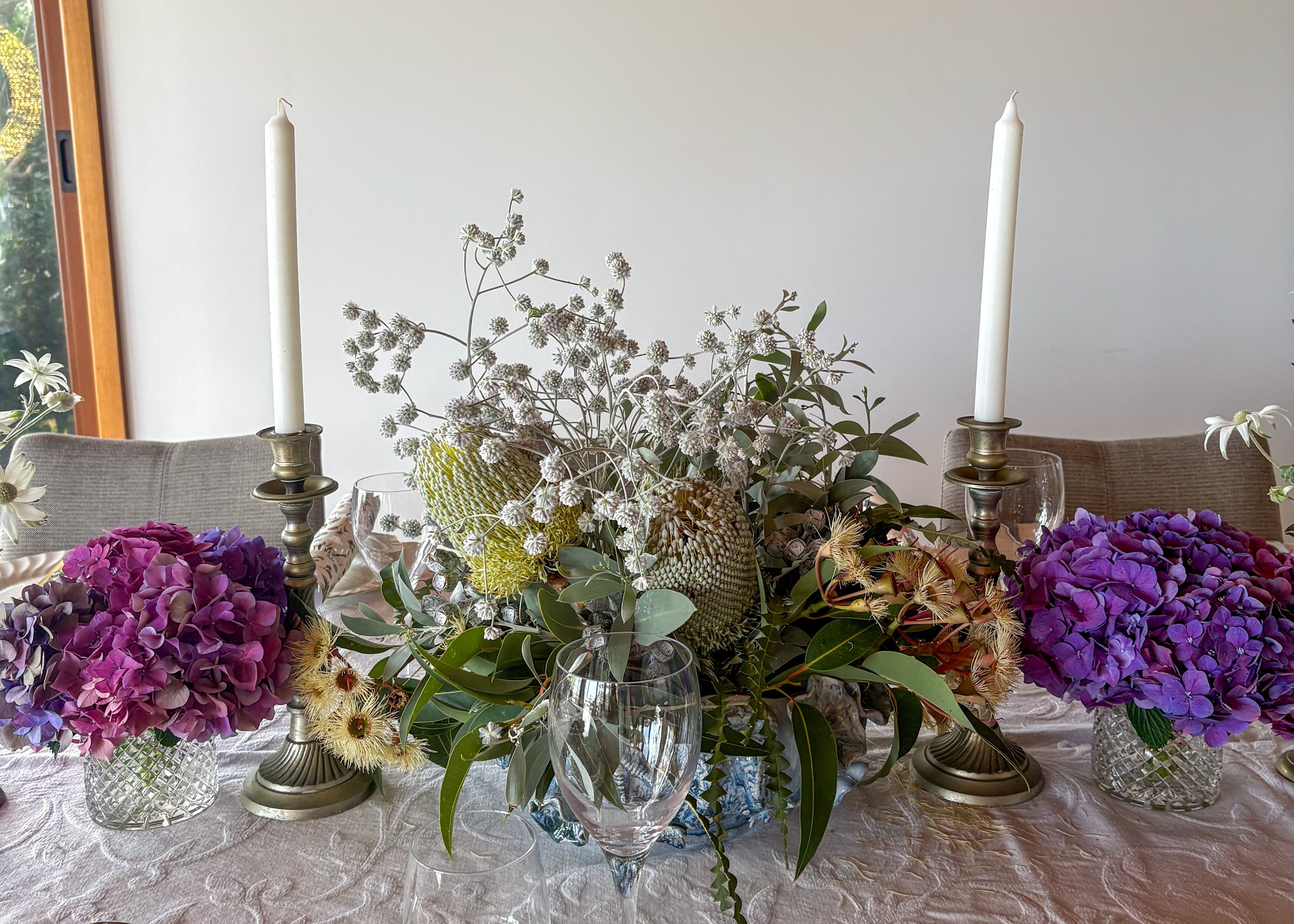 Dining table set with floral arrangements, candles, and cutlery on a white tablecloth.