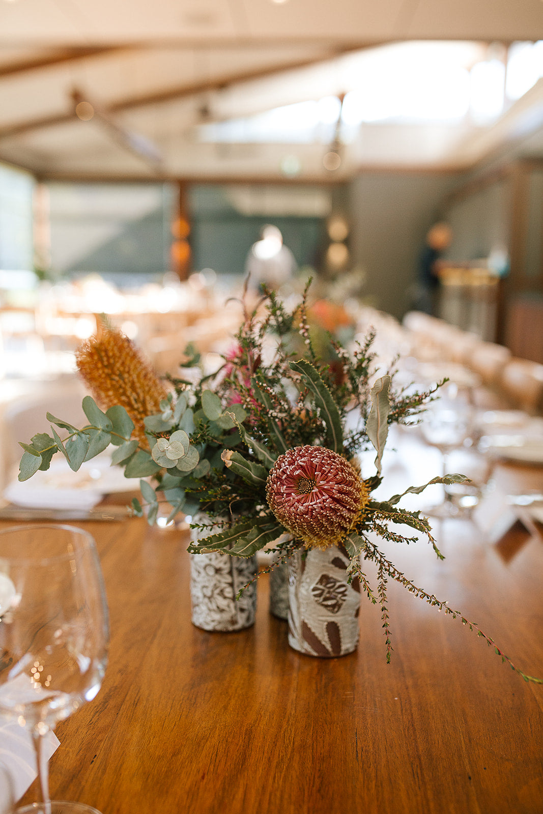 Floral vase arrangement on a wooden table with chairs in the background