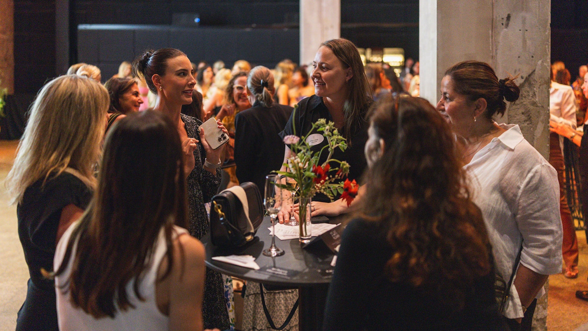 Group of women socializing at a formal event with a table and floral arrangement.