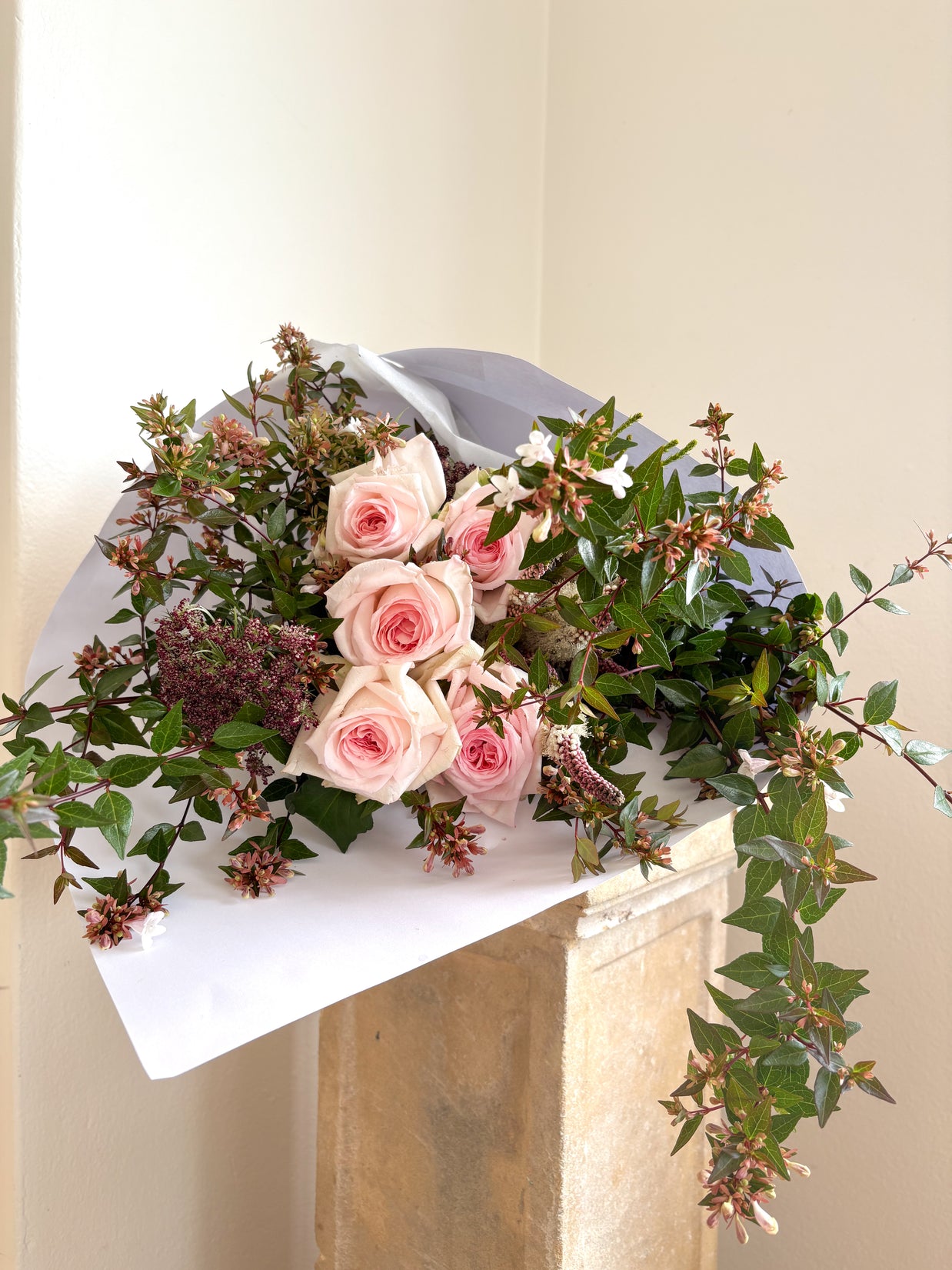 Bouquet of pink roses and greenery on a white surface with a neutral background