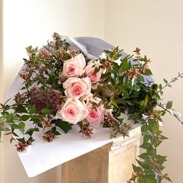 Bouquet of pink roses and greenery on a white surface with a neutral background