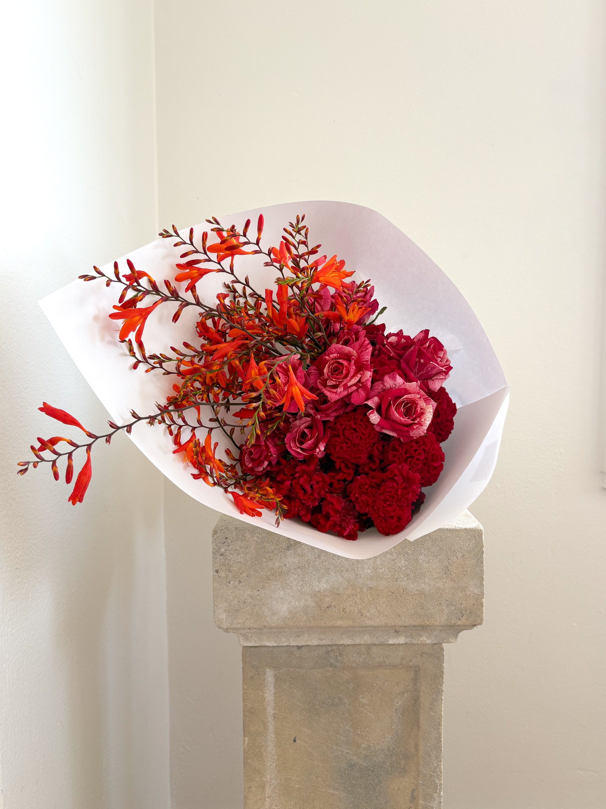 Bouquet of red, pink and orange flowers on a stone pedestal against a white wall
