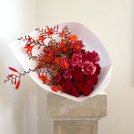Bouquet of red, pink and orange flowers on a stone pedestal against a white wall